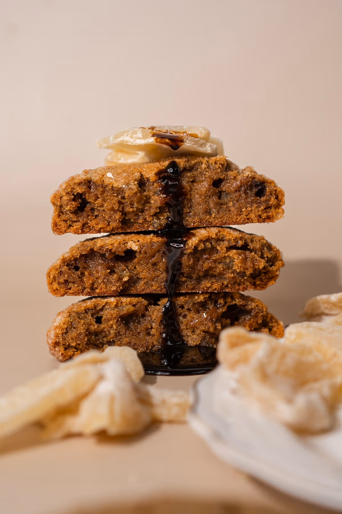 Stack of three molasses ginger cookies with syrup dripping between layers and dried banana chips on top.