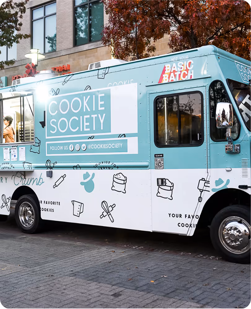 Blue and white Cookie Society food truck with baking-themed illustrations parked on a city street.