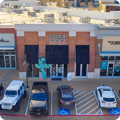 Brick storefront of Cookie Society with black awnings and a blue balloon sculpture outside.