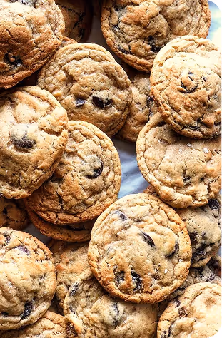 Close-up of a pile of freshly baked chocolate chip cookies on a white surface.