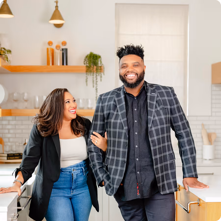 Smiling couple standing together in a modern kitchen with white countertops and shelves.