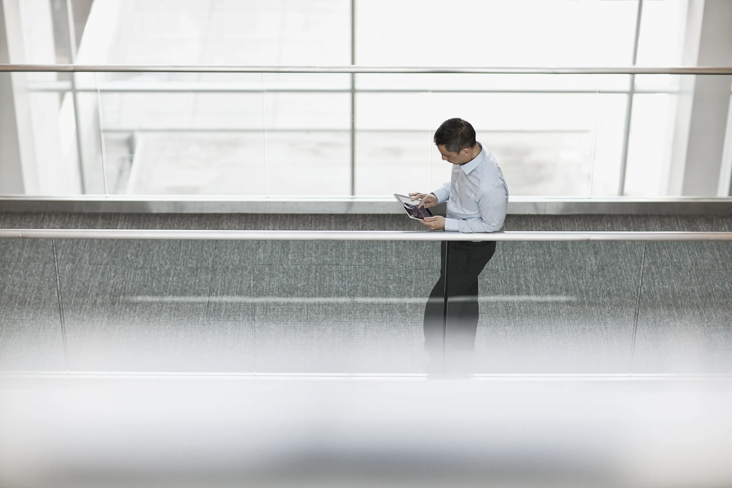 Focused businessman using a tablet while leaning on an office railing