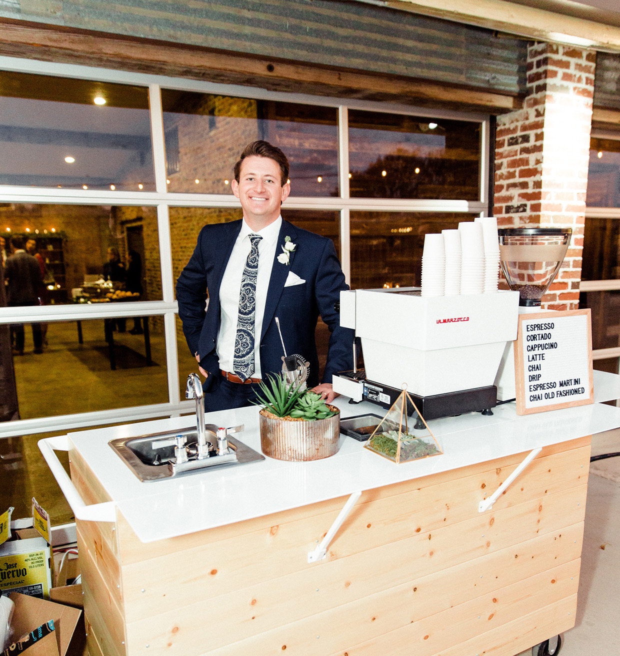 Nightowl barista standing behind a wooden coffee cart at an indoor event.