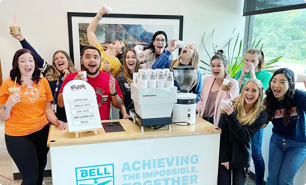 Group of people celebrating at a Bell-branded event, holding a sign and smiling.