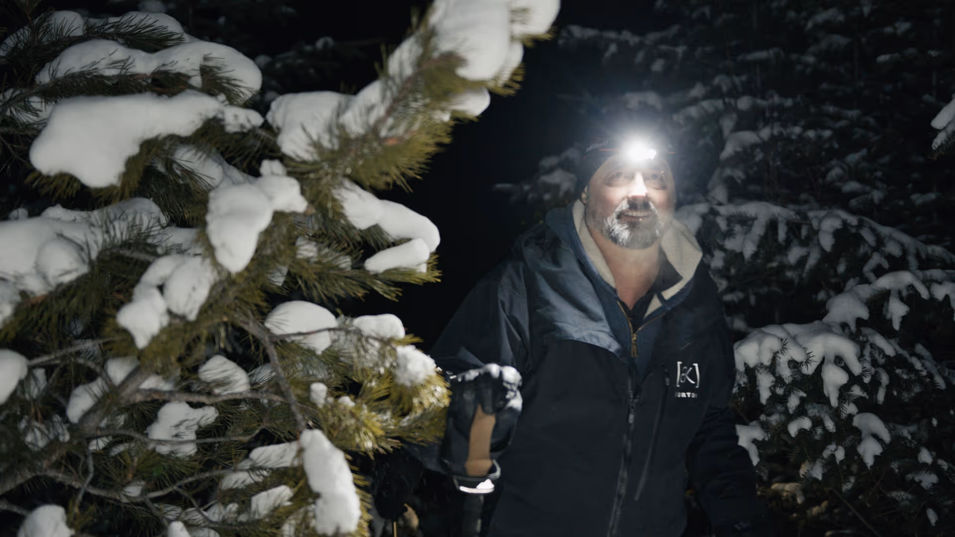 Man wearing Burton [AK] jacket hiking through a snowy forest.