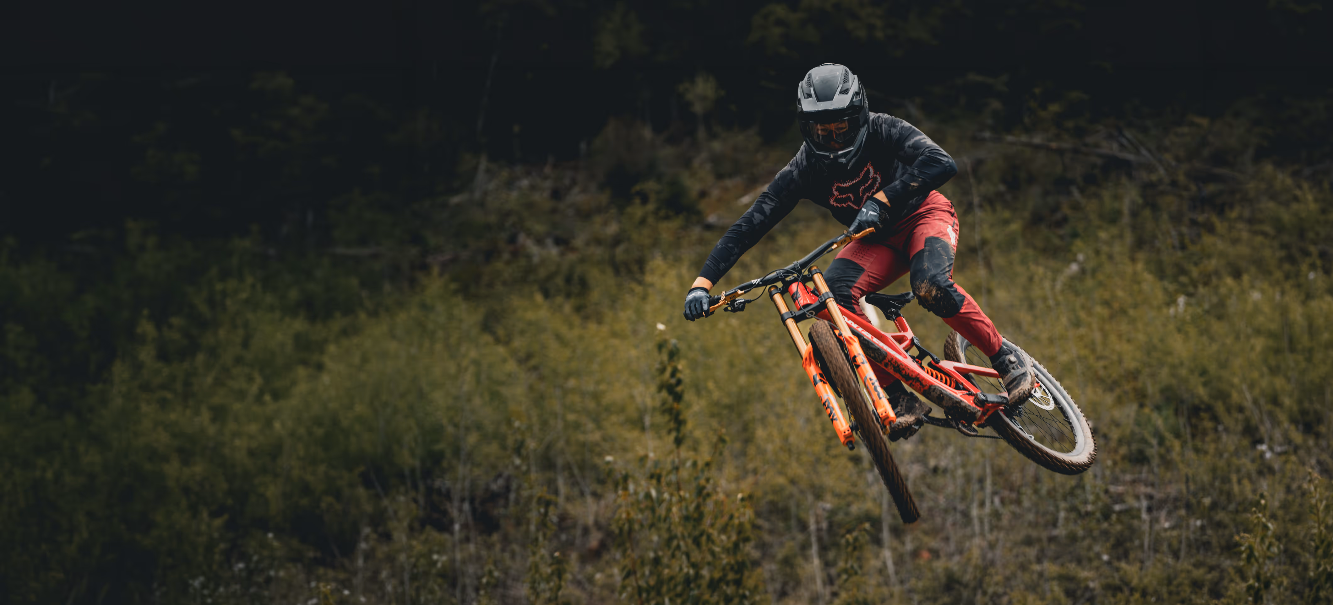 Downhill MTB racer throwing a whip over a jump.