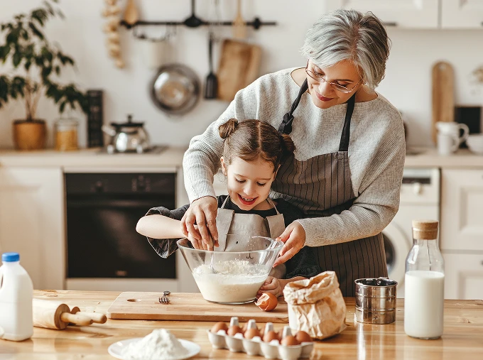 Retired woman and grand-daughter baking together, mixing ingredients in a glass bowl in a kitchen.