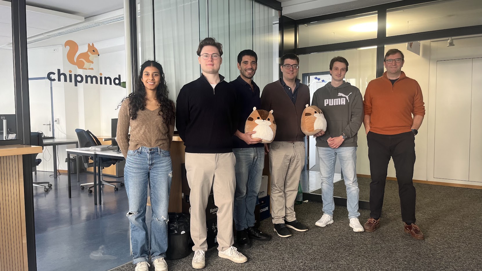 Six people standing in an office near a glass wall with a chipmind logo holding plush toys.