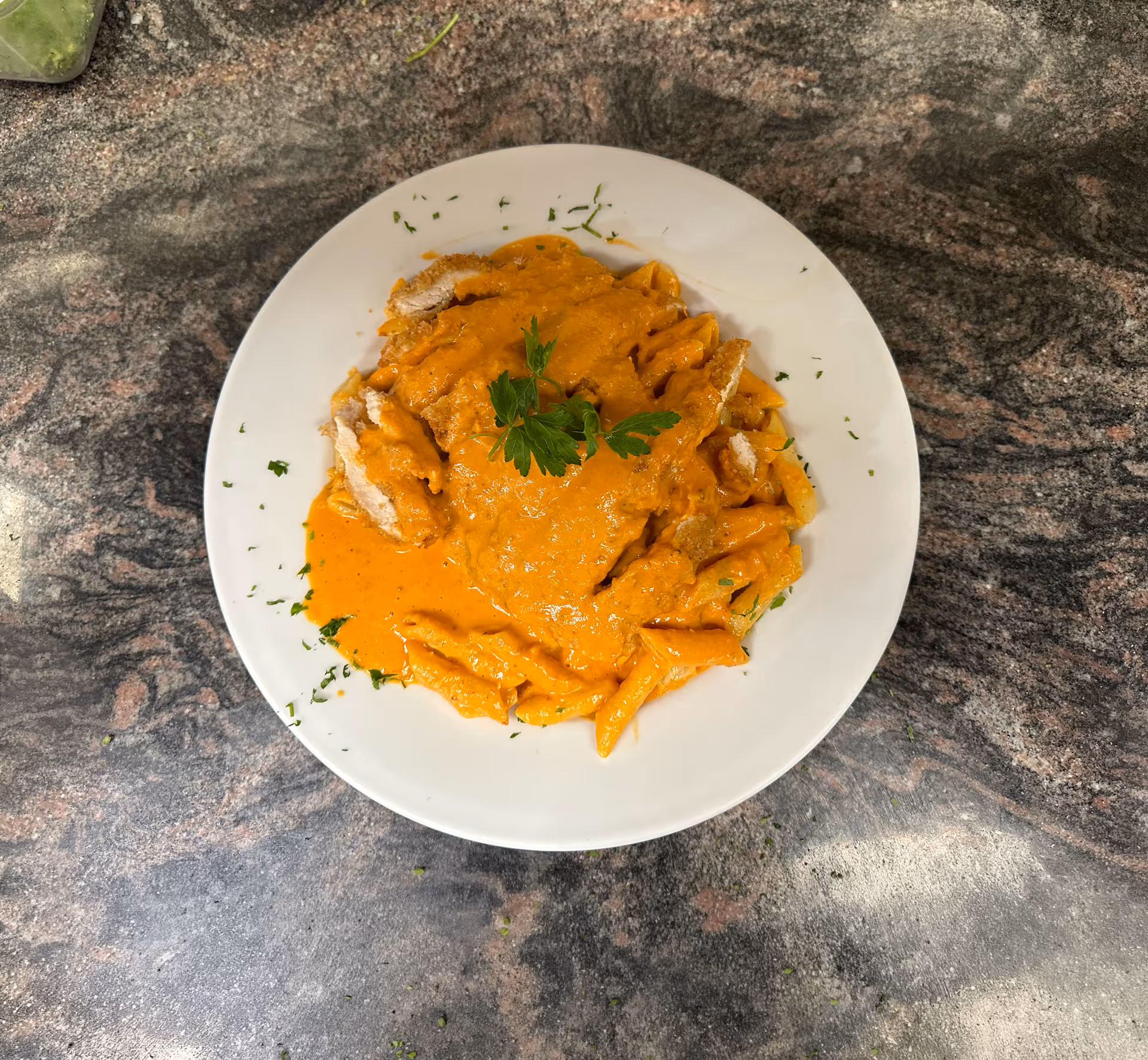 Person spreading red tomato sauce on pizza dough on a floured countertop in a kitchen.