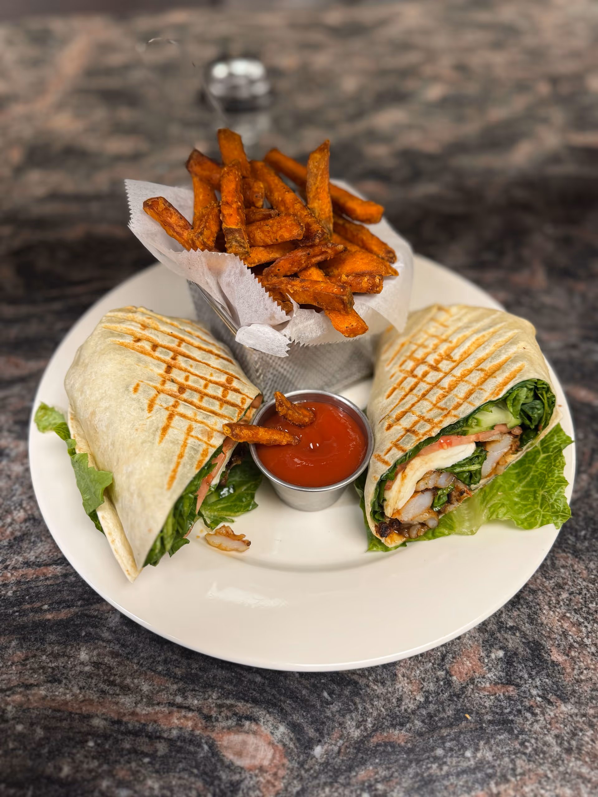 Grilled wrap sandwich halves with lettuce, shrimp, and tomato, served with sweet potato fries and ketchup.