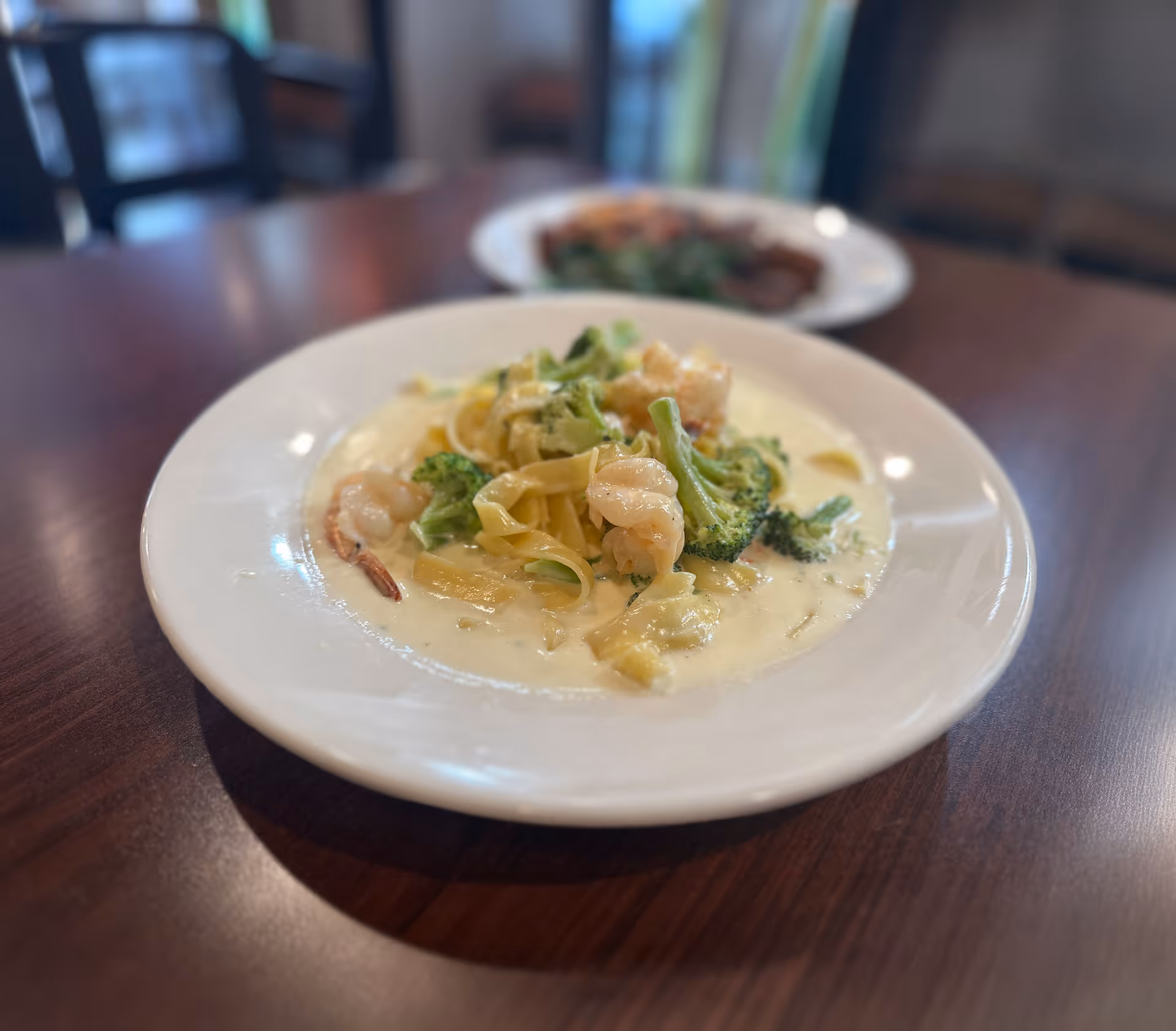 Creamy shrimp pasta with broccoli on a white plate on a wooden table.