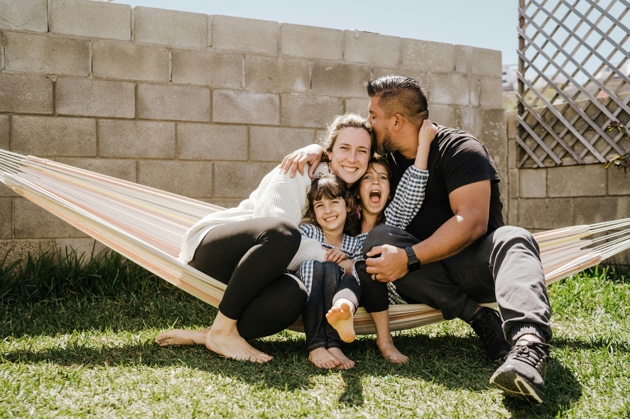 Family of four laughing together in a hammock in their backyard