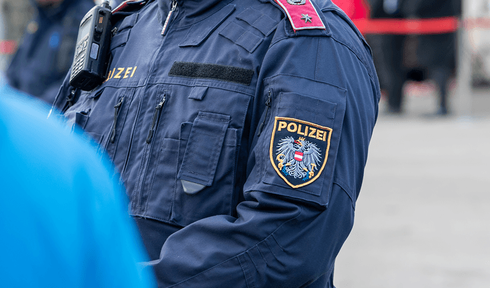 Nahaufnahme eines österreichischen Polizisten in blauer Uniform mit Polizeiwappen.
