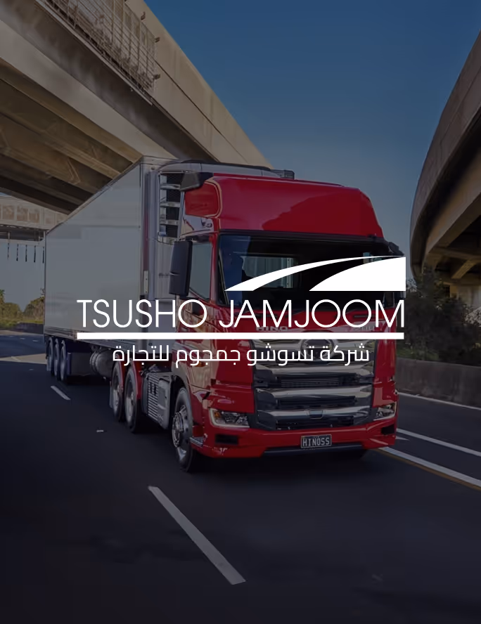 Red semi-truck with white trailer driving on highway under overpasses with Tsusho Jamjoom logo overlay.