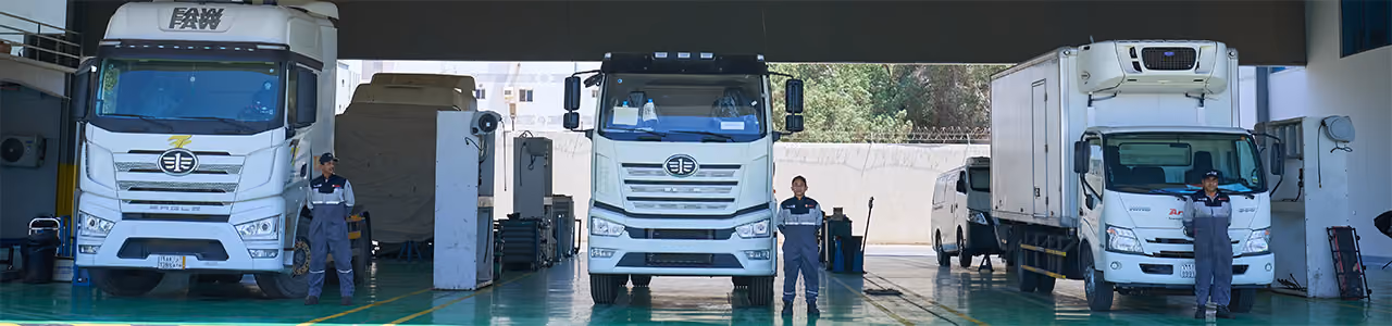Three white trucks parked indoors with three workers standing in front of each truck.