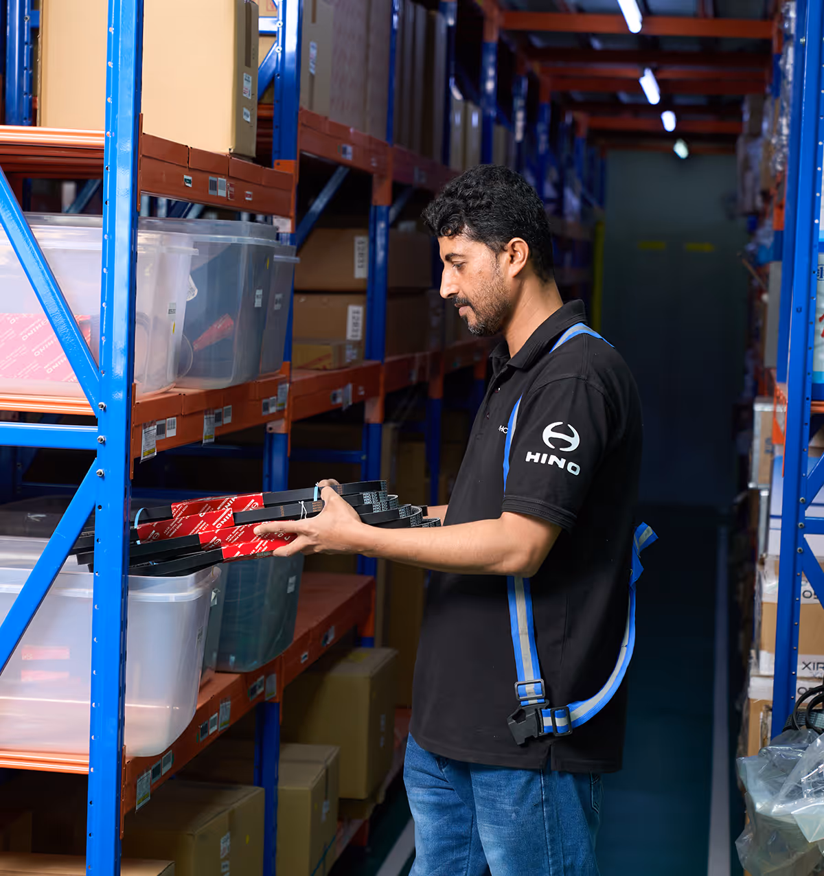 Man in Hino shirt placing automotive parts on shelves in a warehouse aisle.