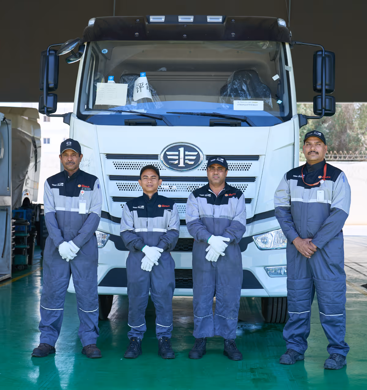 Four men in gray uniforms and white gloves standing in front of a large white truck.