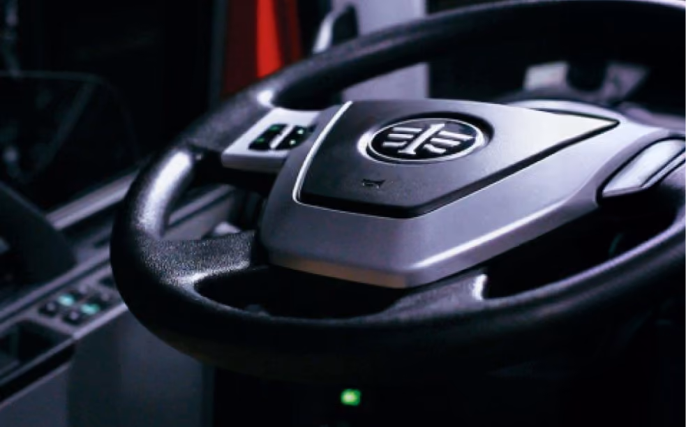 Close-up of a black steering wheel with a central logo and control buttons in a vehicle interior.