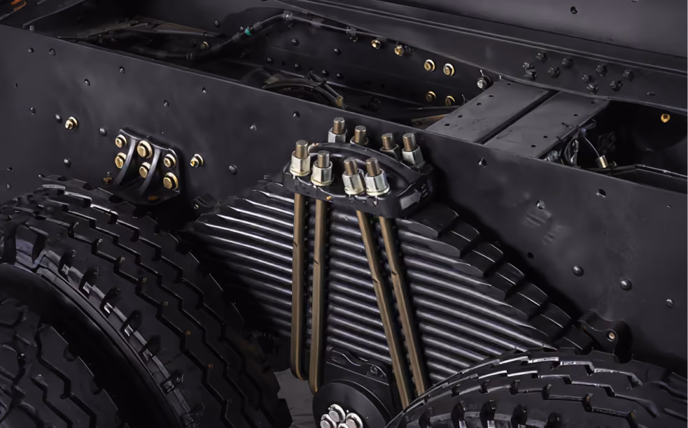 Close-up of black heavy vehicle suspension system with leaf springs and large tires.