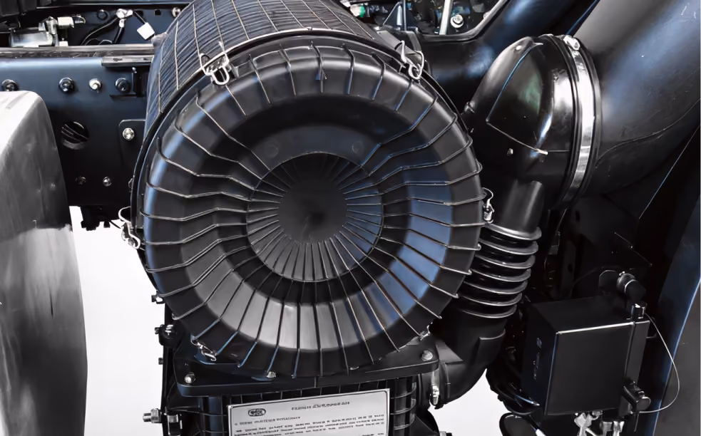 Close-up of a black mechanical engine component with circular air filter and metal clasps.