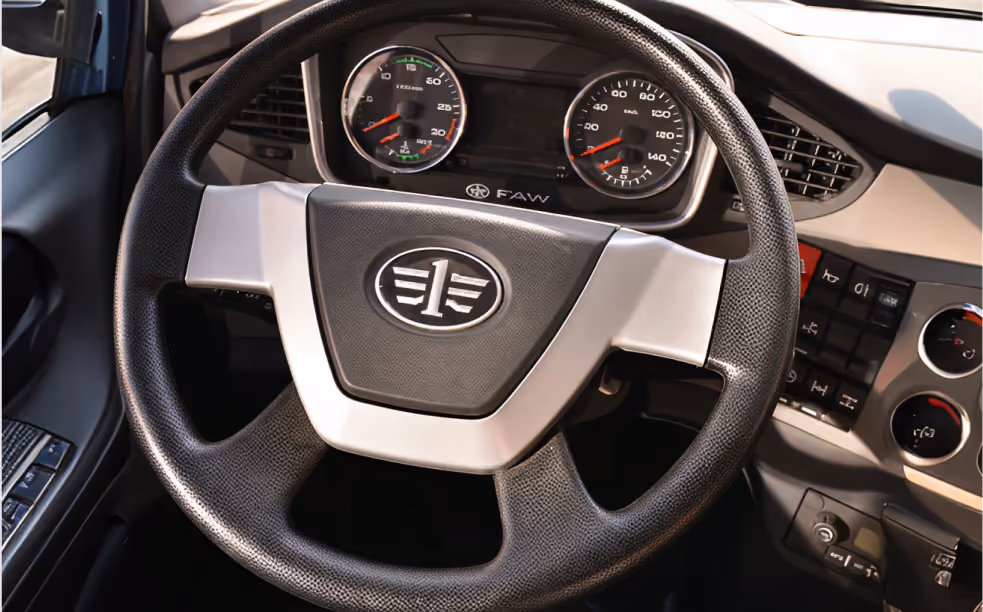 Close-up of a vehicle's black steering wheel with FAW logo and dashboard gauges in the background.