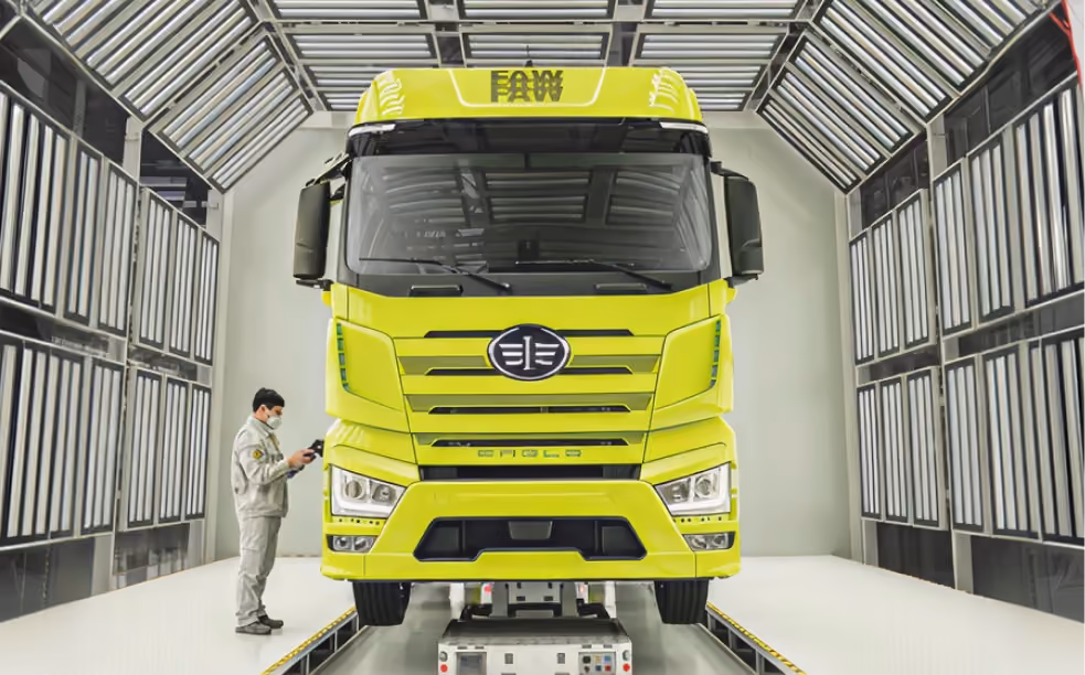 Worker wearing mask inspects bright yellow FAW truck cab inside a modern inspection bay.
