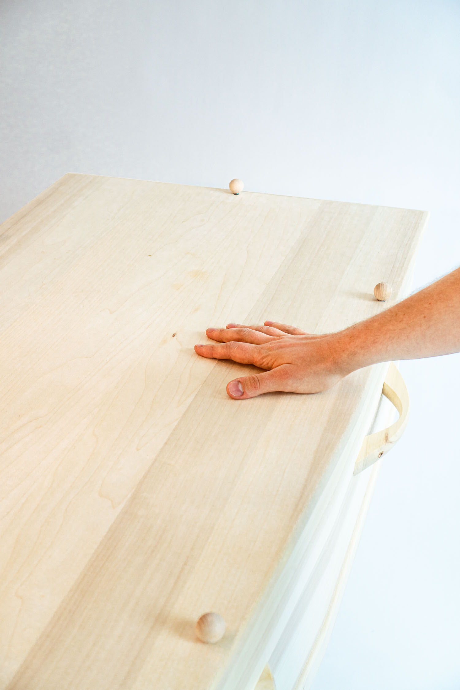Hand resting on a light wooden tabletop with round wooden knobs on the edges.