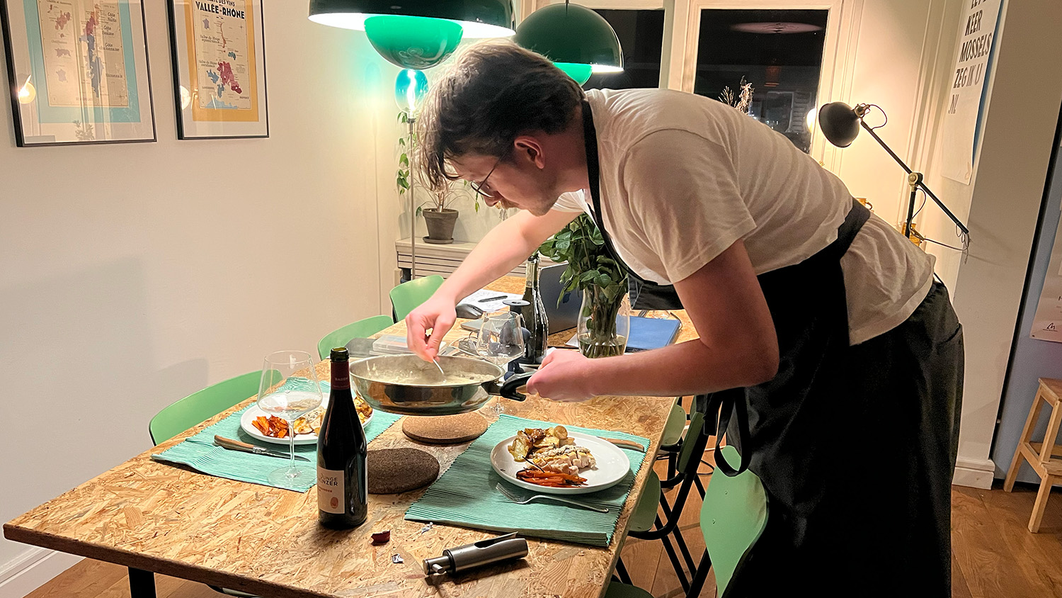Man in wit t-shirt met schort serveert een bord met eten aan de houten tafel in een eetkamer.