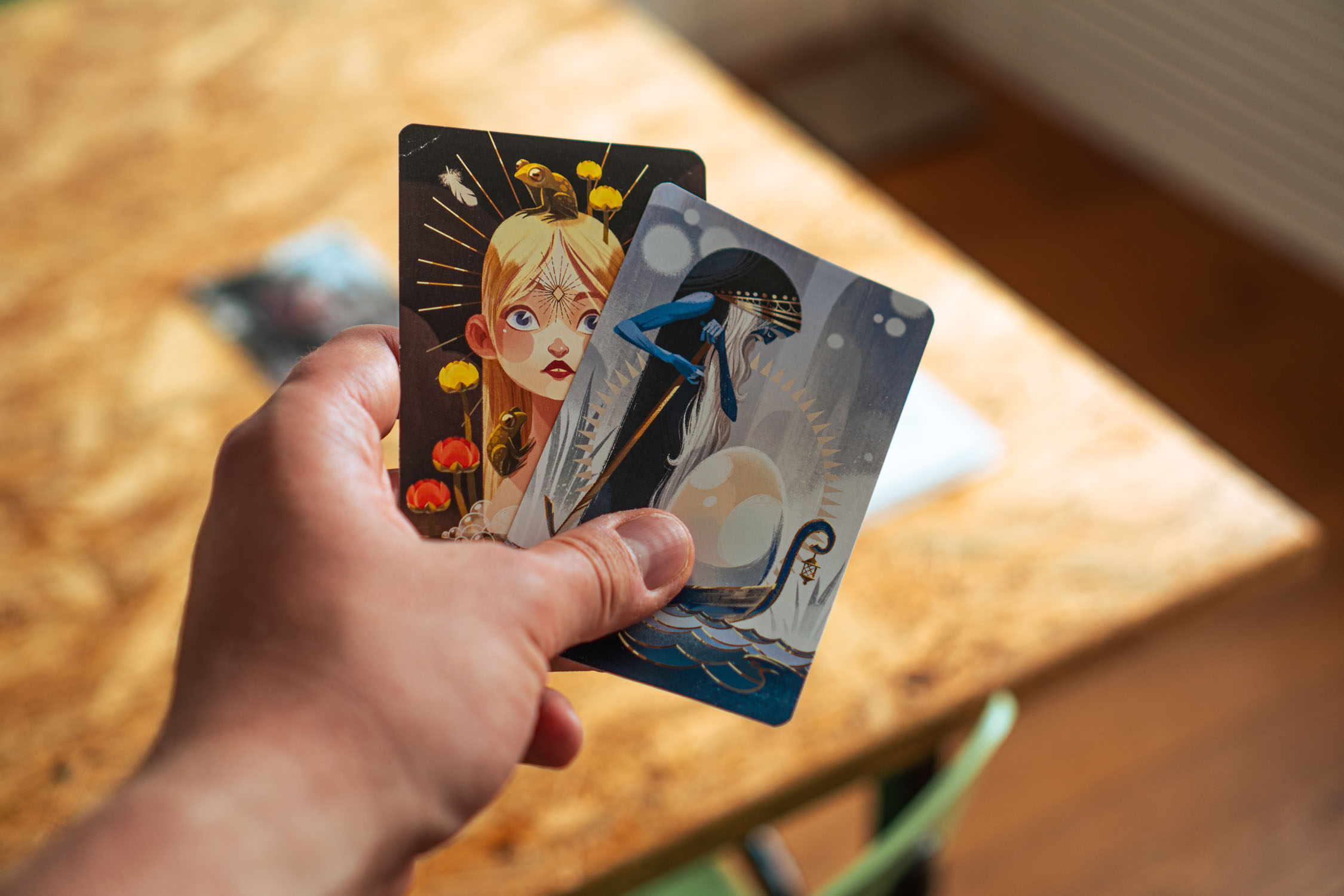Hand holding two illustrated tarot cards showing a blonde woman and a figure in a boat.