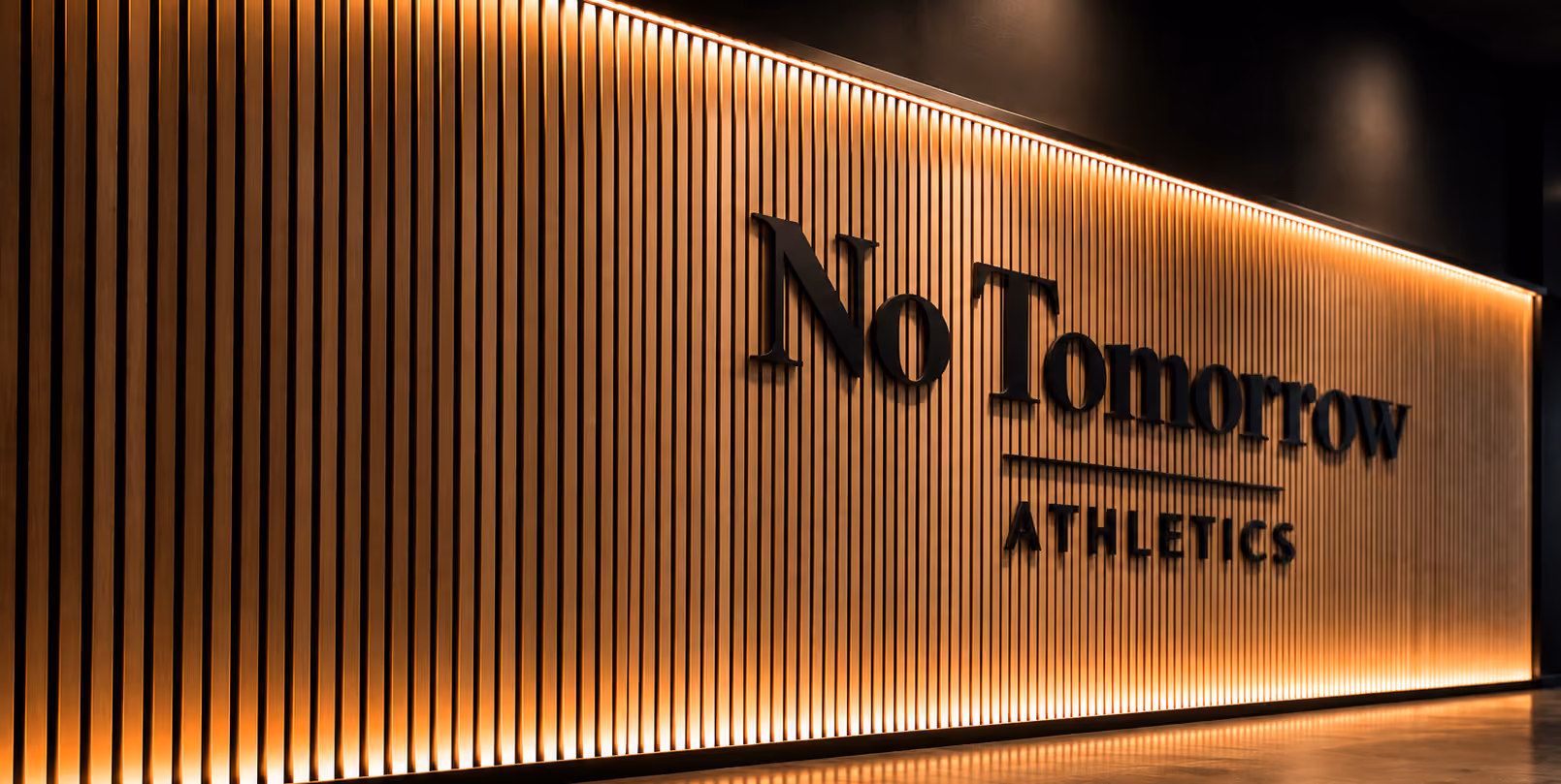Interior wall with vertical wooden slats lit by warm lighting, featuring the black text 'No Tomorrow ATHLETICS'.