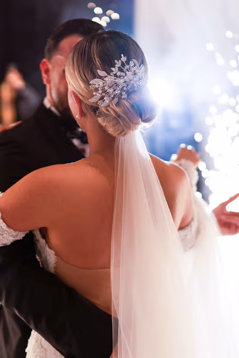 Bride with an elegant hairpiece and long veil dancing with groom at wedding celebration.