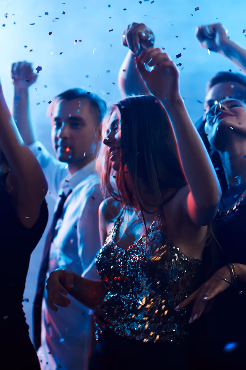 Young people dancing joyfully with confetti falling around in a party atmosphere.