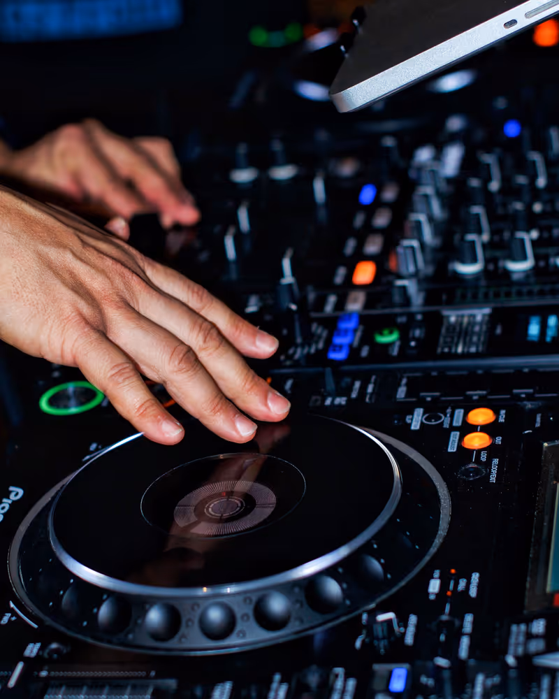 Close-up of DJ hands adjusting controls on a mixing console with lit buttons and knobs.