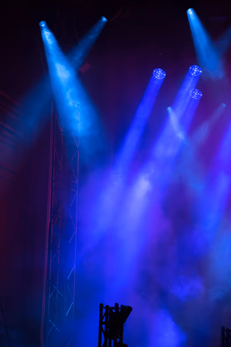 Multiple blue stage spotlights shining through fog in a dark concert or theater setting.