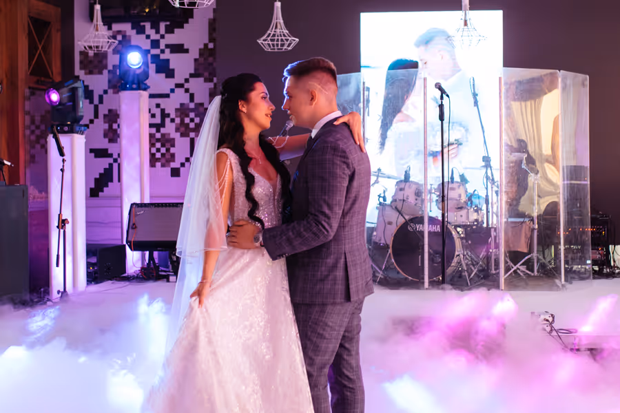 Bride and groom dancing surrounded by smoke on a lit stage during their wedding reception.