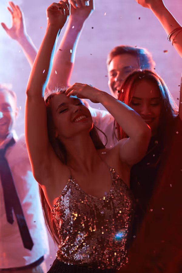 People dancing closely together, smiling and raising hands at a festive party with confetti.
