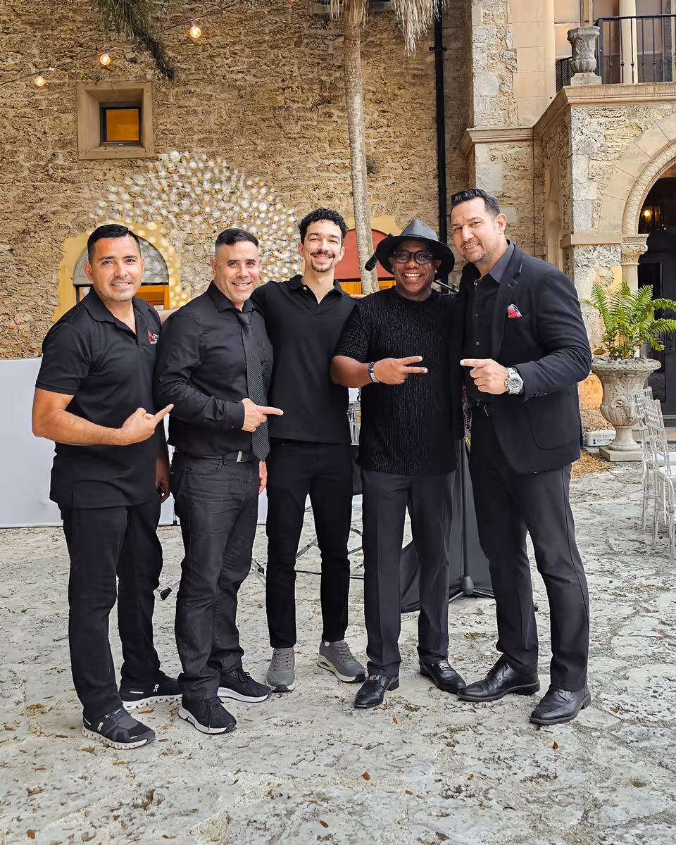 Five men from the Phent Entertainment team standing outside in front of a stone wall, smiling and pointing at the man in the middle.