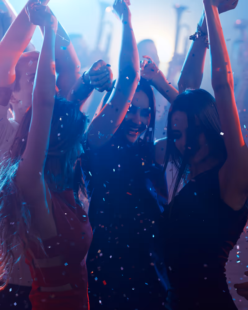 Group of people dancing and celebrating with raised hands and confetti at a party.
