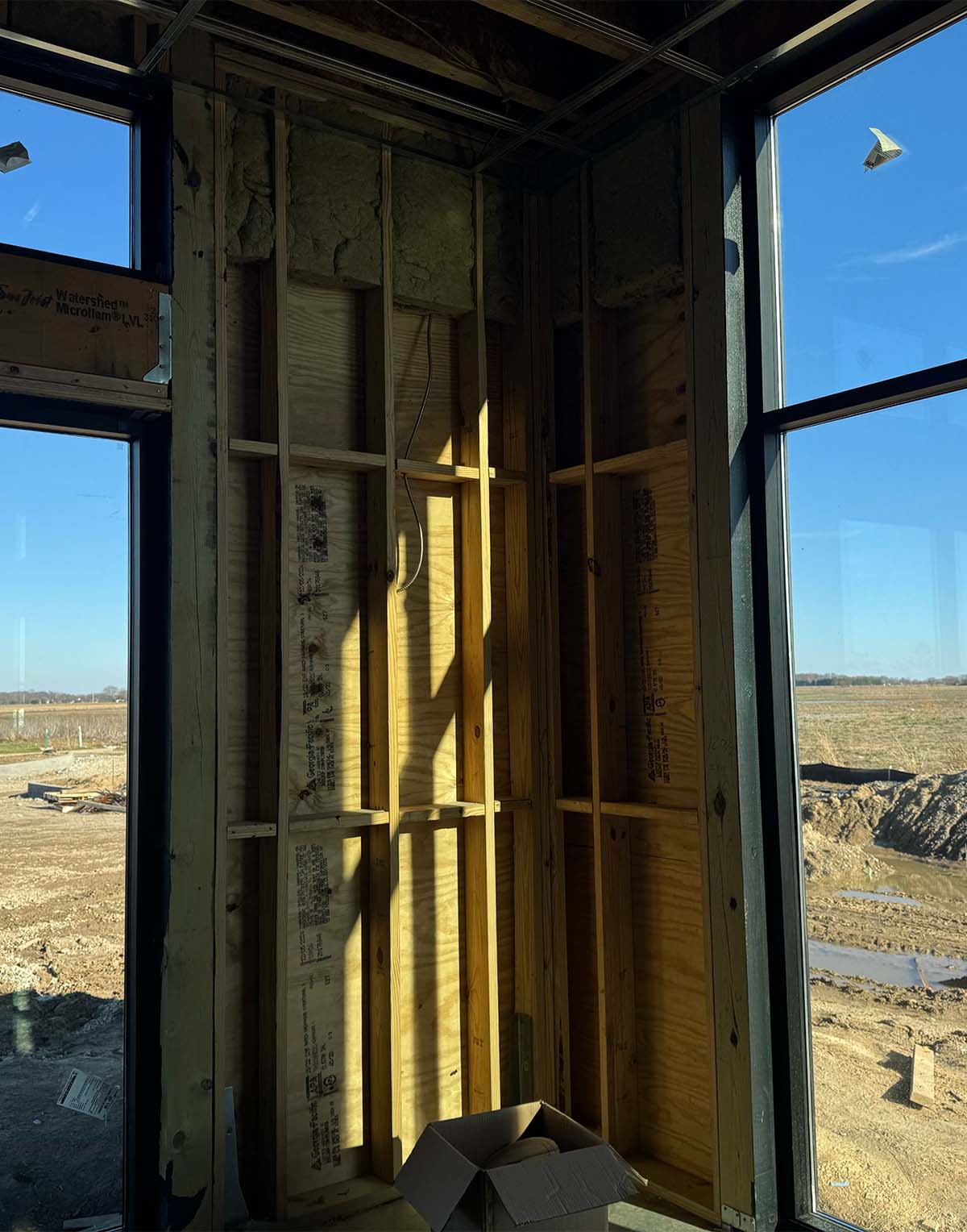 Interior corner of a wooden frame house under construction with sunlight and a cardboard box.