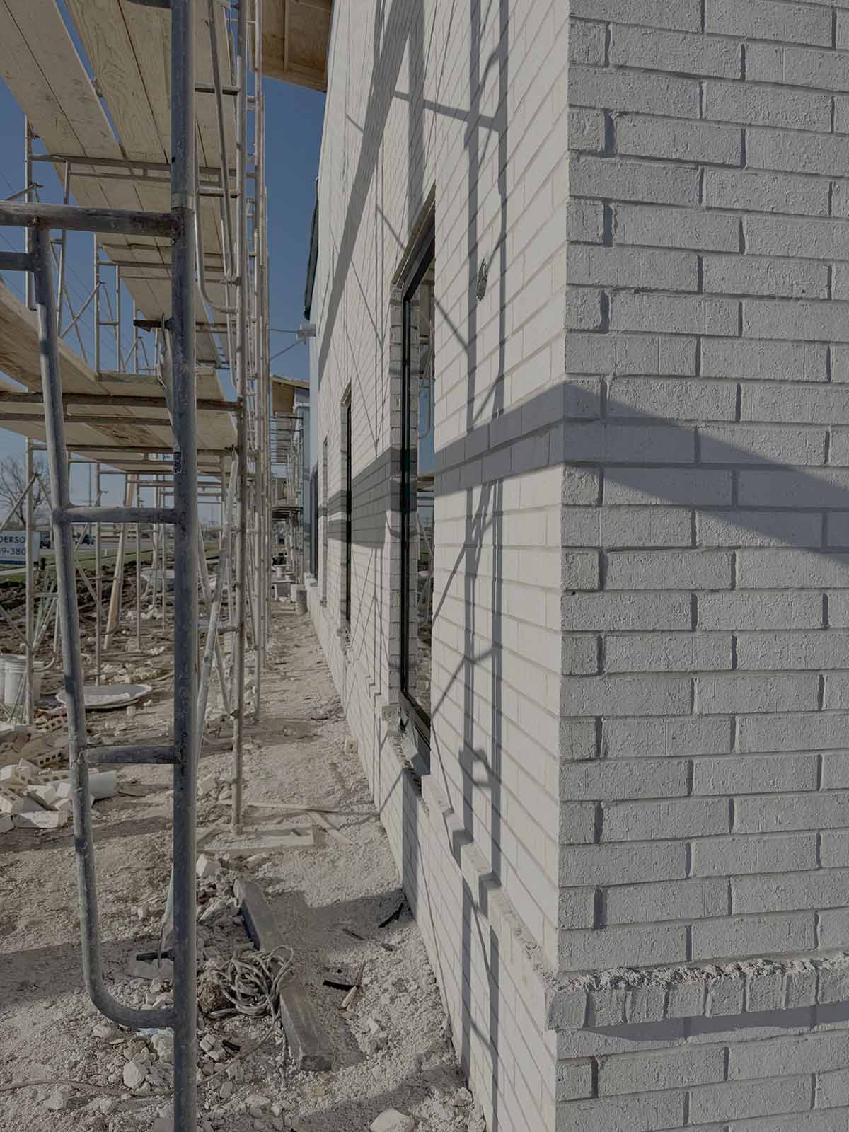 White brick building under construction with scaffolding and shadows on the wall.