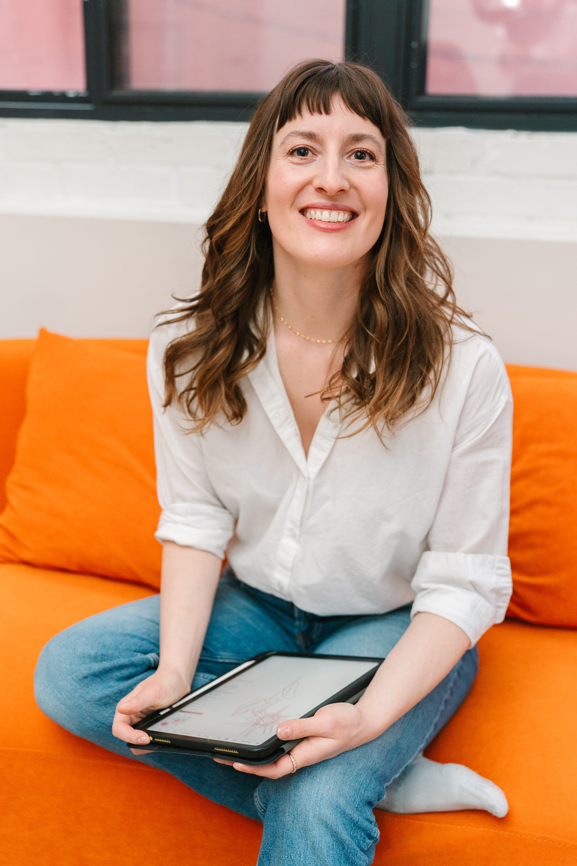 Deanne working on a tablet on an orange couch