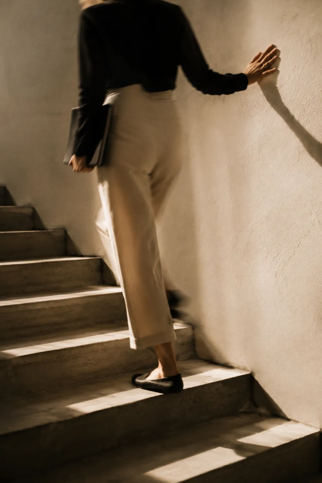 Woman walking downstairs beside a sunlit wall