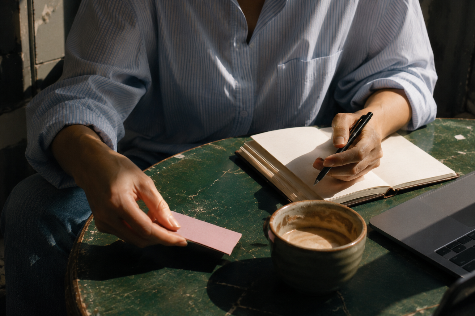 Woman writing in a notebook beside a laptop and coffee
