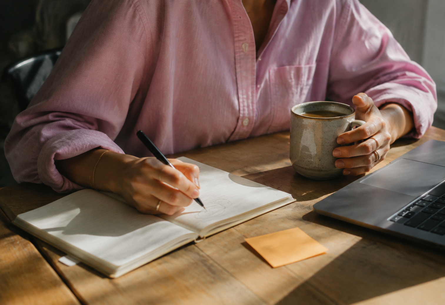 Woman sketching in a notebook beside her laptop
