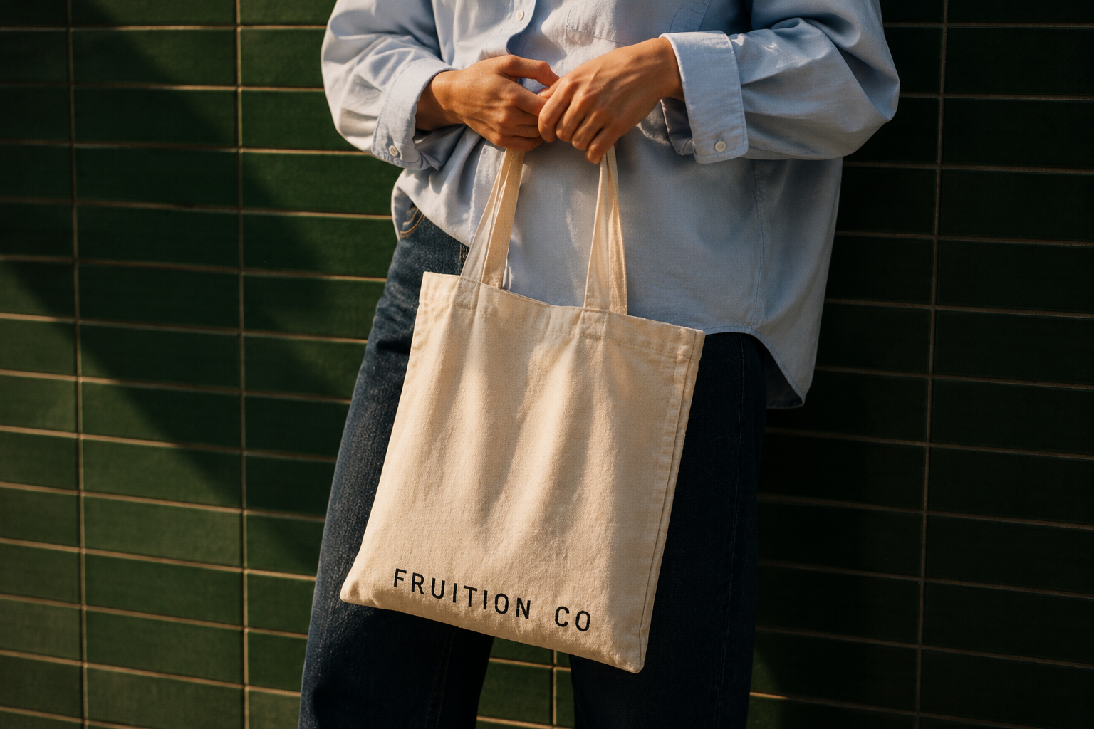 Woman holding a Fruition Co tote bag against green tile