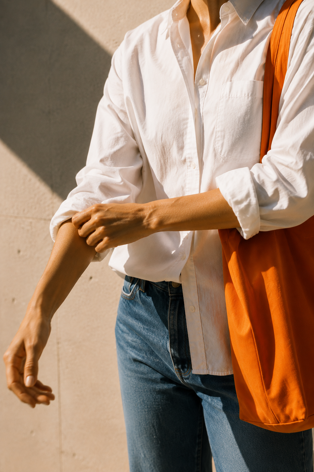 Woman rolling up the sleeve of a white shirt with an orange tote