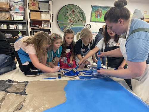 Children and a teacher working together on a large fish print at a studio table