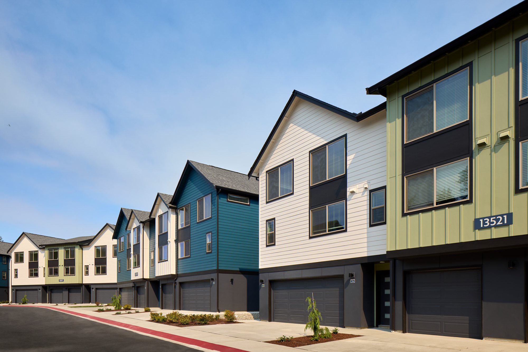 Row of modern townhouses with multiple stories, featuring garages on the ground level and large windows, under a blue sky.