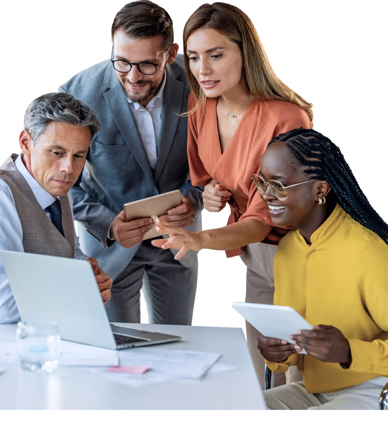 Four diverse colleagues smiling and collaborating over laptops and tablets at a desk.