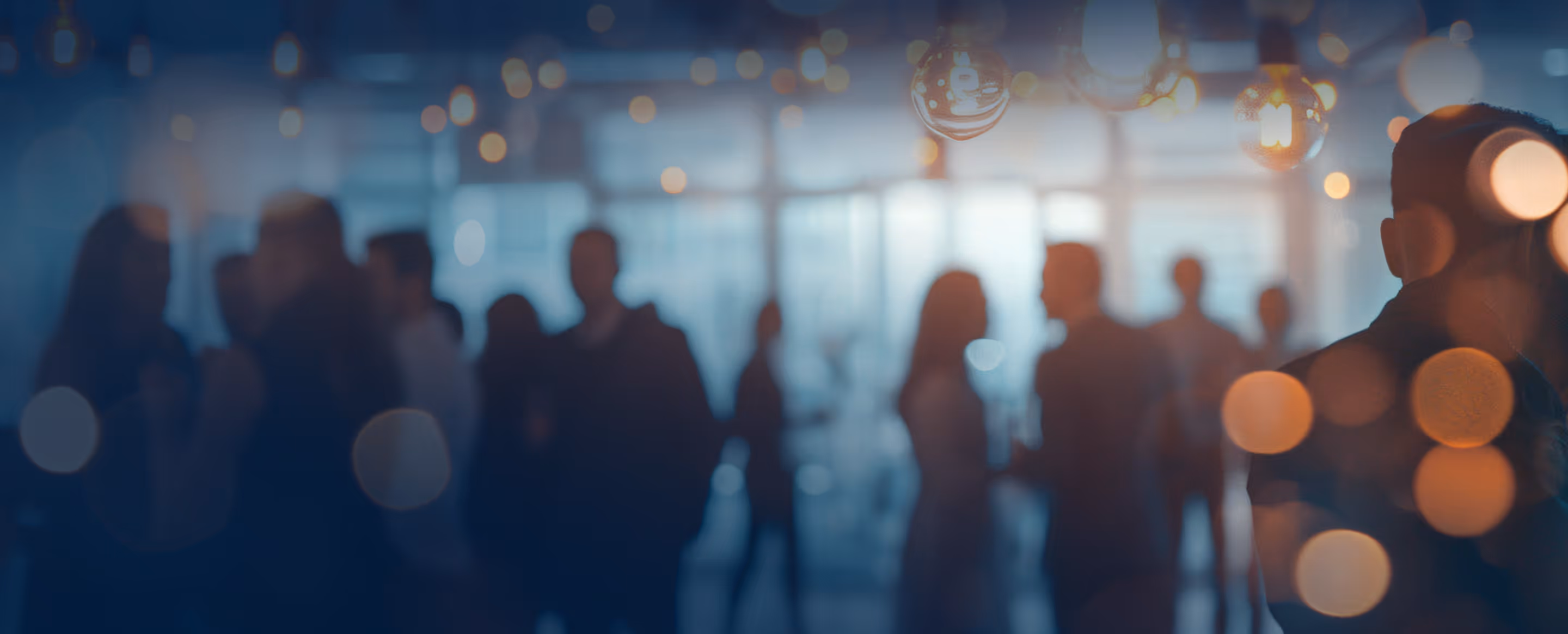 Blurred silhouettes of people socializing indoors with warm hanging lights and bokeh effects.